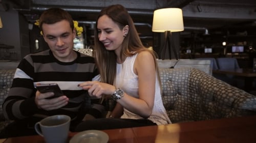 Attractive Young Couple Talking and Using Smartphone at Cafe