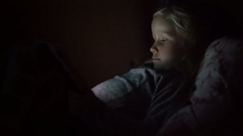 Fille de cinq ans à la recherche de dessin animé allongé sur le canapé dans le noir