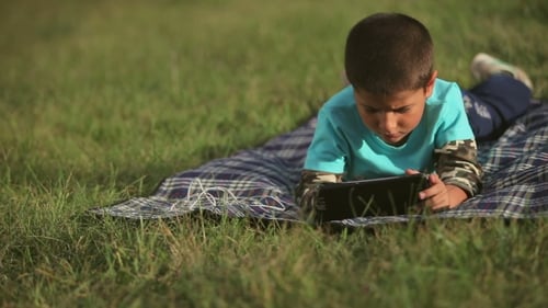 Boy Playing On The Lawn With a Tablet