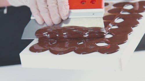 Herstellung von Pralinen, Süßigkeiten. Überschüssige Schokolade aus der Form entfernen.