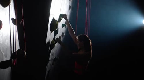 Side View Female Climber Training on a Climbing Wall Practicing Rockclimbing and Moving Up Climbs