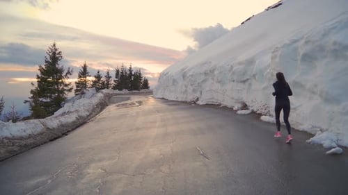 Confident Female Jogger Running on Asphalt Road Reflecting Golden Sunset in the Mountains
