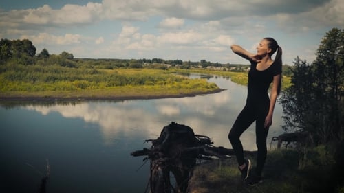 Woman Stretching by a River on a Sunny Day