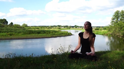 Woman Meditating by River on Sunny Day