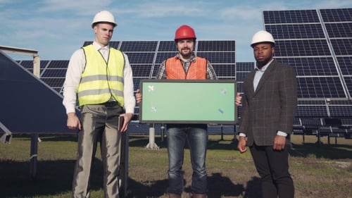Three Engineers Standing Near Solar Panels Holding Sign