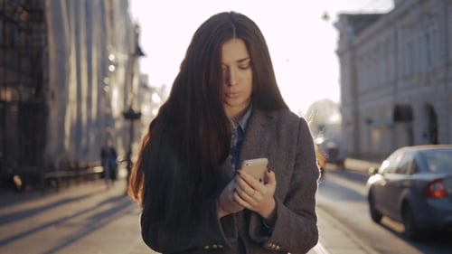 Femme heureuse marchant et utilisant un téléphone intelligent dans la rue en automne. Fille étudiante sexy avec mobile