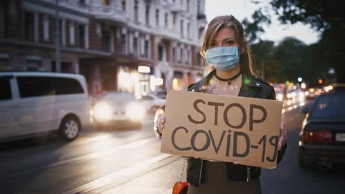 Blonde Woman Holds Stop Covid-19 Sign in City