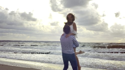 Man Lifts Woman at the Beach by the Ocean