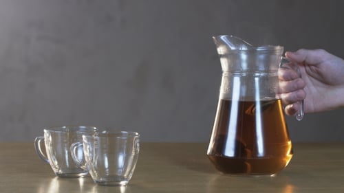 Pouring Hot Tea from Glass Pitcher into Mug