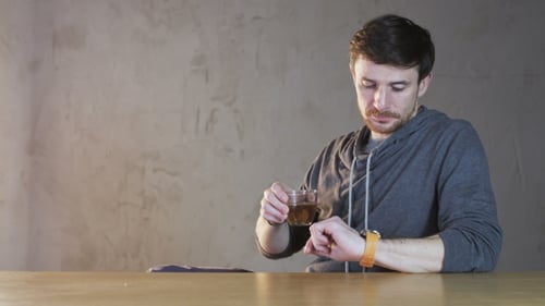 Man with Drink Looks at His Watch Indoors