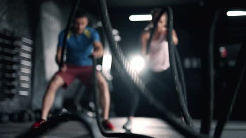 A Fitness Athletes are Training Using Battle Ropes in the Dark Gym