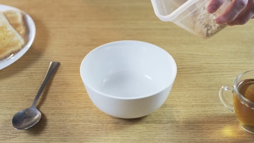 Granola Being Poured Into Bowl At Breakfast Table