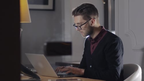 Multitâche. Beau jeune homme portant des lunettes et travaillant avec un ordinateur portable tout en étant assis dans le moderne