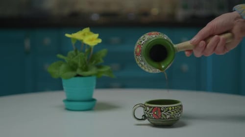 Hand Pours Coffee Into Patterned Cup Indoors