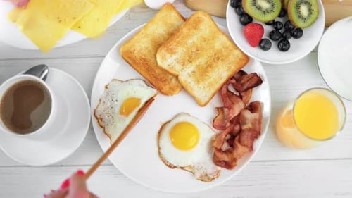 POV Shot Female Hand Adding Fried Egg on Plate with Fresh Tasty Bacon and Toast Food Top View