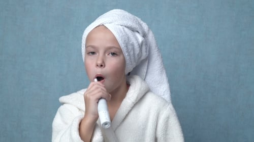 Girl in Robe Brushing Teeth with Electric Toothbrush