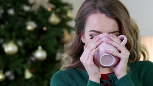 Woman Smiling and Drinking Coffee Near Christmas Tree