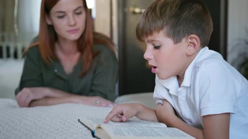Boy Reading Book While Mother Watches