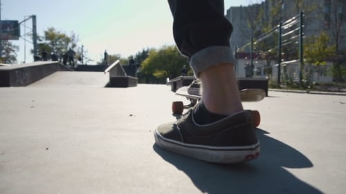 Skateboarder steps onto skateboard in urban skatepark