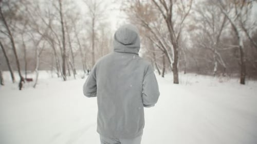 Man runs through the park winter in hoodie, back view, close-up. Young man is jogging winter park.