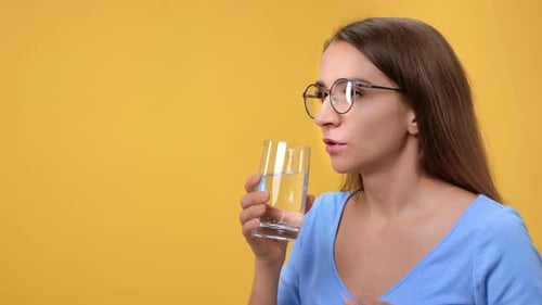 Woman Takes Pill with Water, Yellow Background