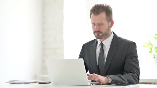 Young Businessman Thinking While Working on Laptop in Office