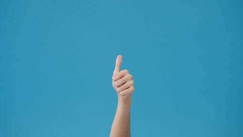 Young woman hand showing thumb up sign with fingers isolated over blue background in studio.