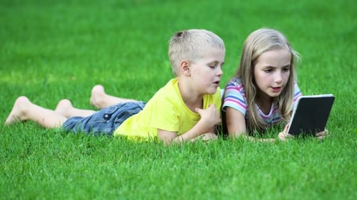 Kids Lying on Lawn Looking at Tablet