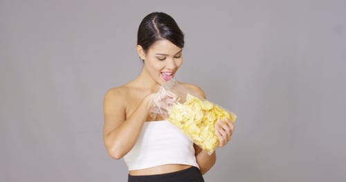 Woman Eats Chip from Bag, Gray Background