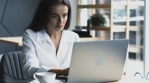 Confident and Beautiful Freelance Woman Working on Laptop in Cafe with Cup of Coffee