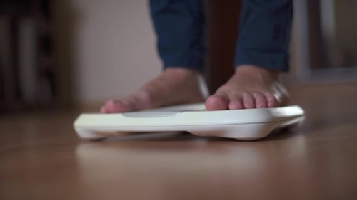 Young Woman Measuring Body Weight On Weighing Scale At Home