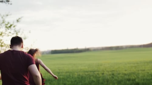 Man Chases His Woman Cheerfully Running in a Field. Happy Lovers Have Fun. Soft Sunset Lights