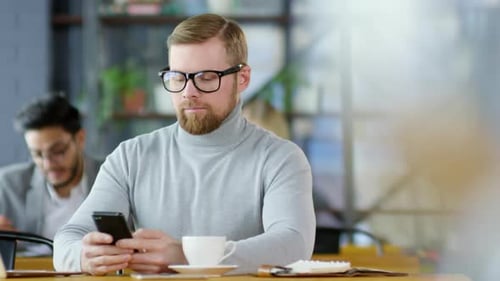 Young Businessman Texting on Smartphone in Coffeeshop