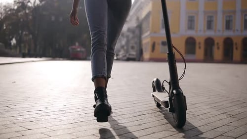Stylish Woman Pulling Electric Scooter in City