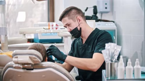 Young Man Dentist Checking the Mouth of a Boy - Looking Back in the Camera