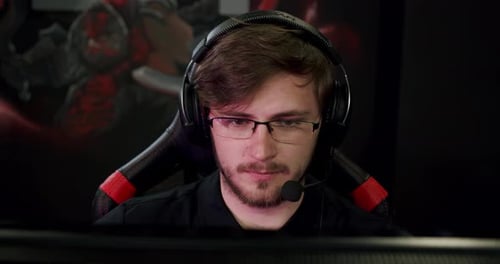 Young Adult Gamer Concentrates, Wearing Headphones and Eyeglasses