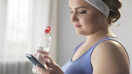 Young Woman with Smartphone and Water Bottle Indoors