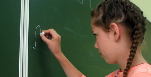 Girl Writes Alphabet on Green School Chalkboard