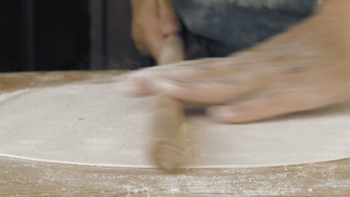 Rolling Dough With a Rolling Pin on Wood Surface