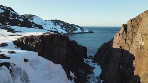 Winter Aerial Flight Through Scenic Canyon Top Over Waves Rolling on Artic Ocean Shore with Round