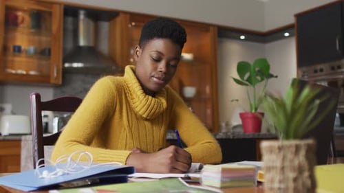 Young Adult Woman Writing at Table in Kitchen