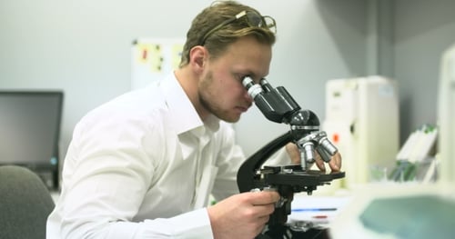 El científico está mirando a través del microscopio y escribiendo datos en la tableta.