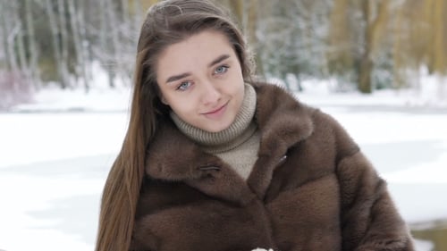 Jolie fille en manteau de fourrure posant dans le parc en hiver. Lentement
