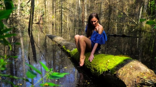 Woman Sits on Mossy Log in Wilderness Pond