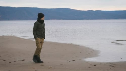 Boy in Warm Clothes Is Walking Along the Coast of Seashore Dreamily Looking at the Water