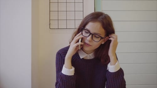 Young Woman Wearing Glasses and Talking on Cellphone in the Cafe