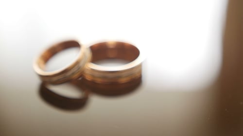 Golden Wedding Rings on Mirror Glasses Table - One Lies Top of Another
