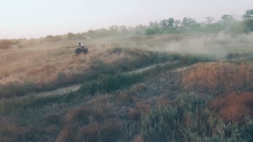 ATV Rider Racing Across Rural Grassy Dunes at Sunrise