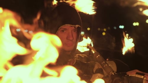 Man in Hoodie with Two Burning Torches at Night