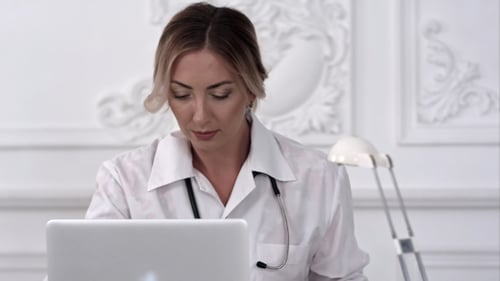 Serious Female Doctor Using Her Laptop Computer in Medical Office